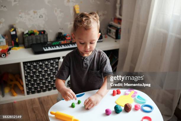 little boy child sitting at table playing with play doh or plasticine at home, sensory indoor activities for toddlers. creativity and play - child play doh stock pictures, royalty-free photos & images