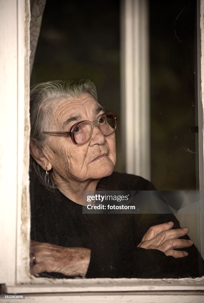 Senior woman standing by the window and looking out
