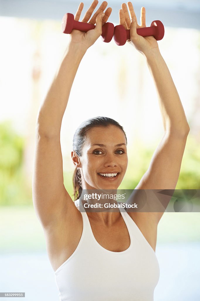 Happy middle aged female with dumbbells doing exercise