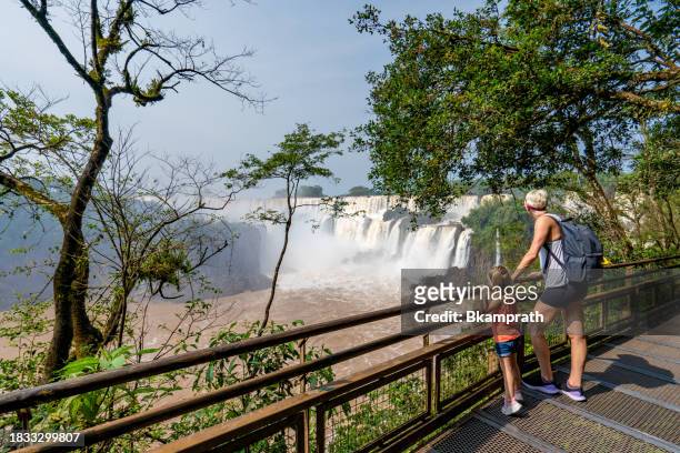 mother and daughter enjoying the breathtaking mighty iguazu falls in iguazu national park on the boarder of argentina and brazil, south america - argentina devils throat stockfoto's en -beelden