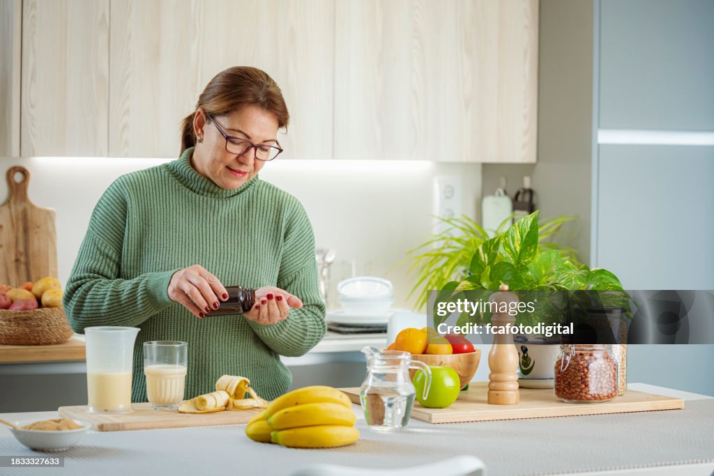 Mature woman standing in her kitchen and taking her vitamins