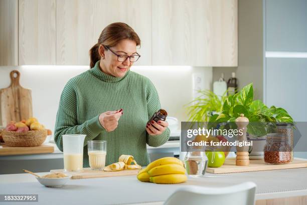 woman in kitchen holding dietary supplement pills bottle - antioxidant stock pictures, royalty-free photos & images