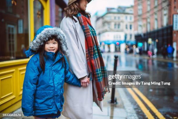 lovely cheerful girl in hooded jacket walking in downtown street with her mom under the rain - retail equipment stock pictures, royalty-free photos & images