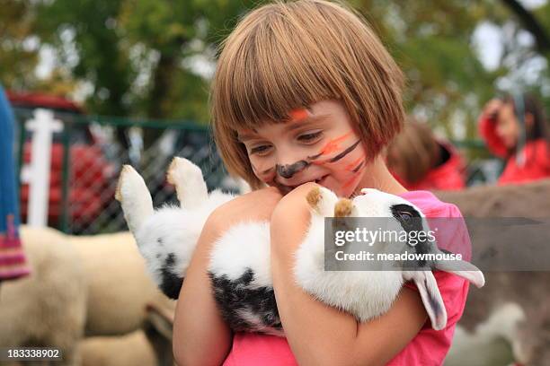 little girl with painted tiger face holds rabbit upside down - kinderboerderij stockfoto's en -beelden
