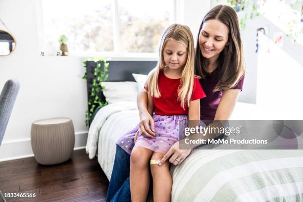 mother putting bandage on young daughters knee in bedroom - beautiful girls legs stock pictures, royalty-free photos & images