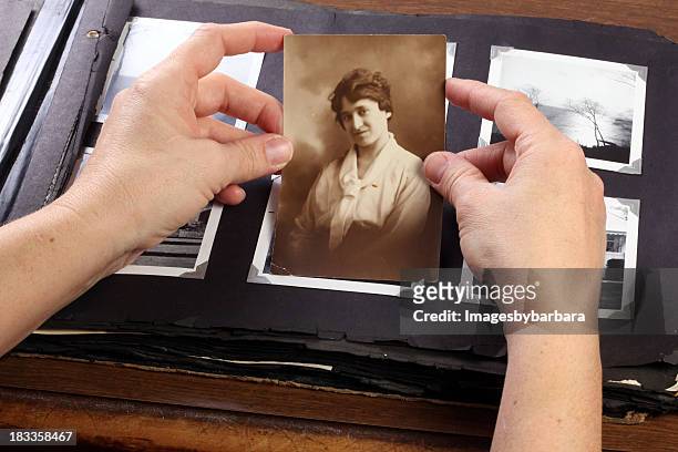hands holding a sepia photograph above a phot album - decades stock pictures, royalty-free photos & images