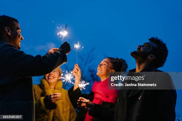 landscape shot of a group of friends standing outside, holding sparklers and looking up at the sky - buon anno foto e immagini stock