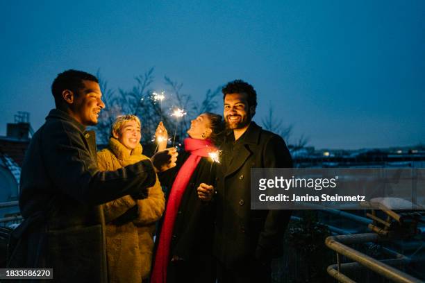 four young friends stand on a terrace in the evening in the city , holding sparklers in their hands - silvester berlin stock-fotos und bilder