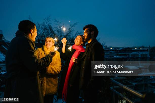 shot of a cheerful group of friends standing on a terrace at night with sparklers in hand - oudjaarsavond stockfoto's en -beelden