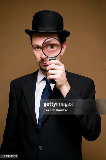 homme avec chapeau melon regardant à travers une loupe - détective photos et images de collection