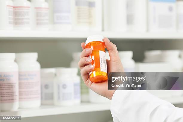 pharmacist holding a bottle of prescription medication in pharmacy - prescription drug bottle stock pictures, royalty-free photos & images