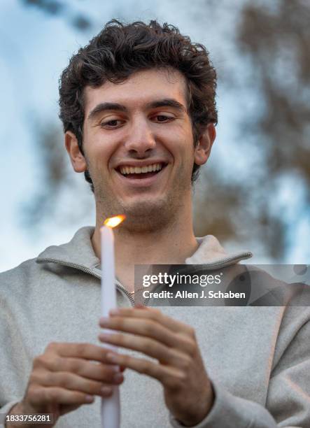 Los Angeles, CA USC student Caleb Ouanounou holds the first candle to be placed on a menorah ice sculpture as the Chabad Jewish Student Center at USC...