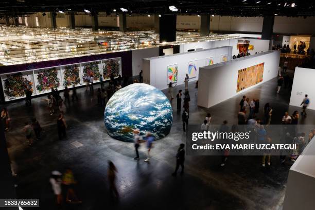 Visitors walk by a giant earth globe during the 21st edition of Art Basel at the Miami Beach Convention Center in Miami Beach, Florida, on December...