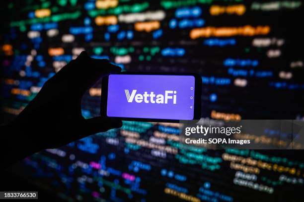 In this photo illustration a VettaFi logo is displayed on a smartphone with stock market percentages in the background.