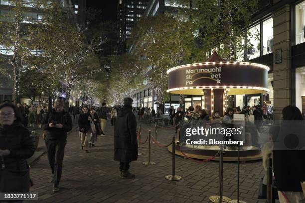 People sit on a carousel in the Marunouchi area of Tokyo, Japan, on Friday, Japan, on Dec. 8, 2023. Inflation data are well above the Bank of Japan's...