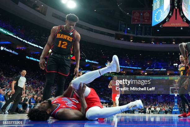 Joel Embiid of the Philadelphia 76ers grabs his leg after an injury in front of De'Andre Hunter of the Atlanta Hawks in the fourth quarter at the...