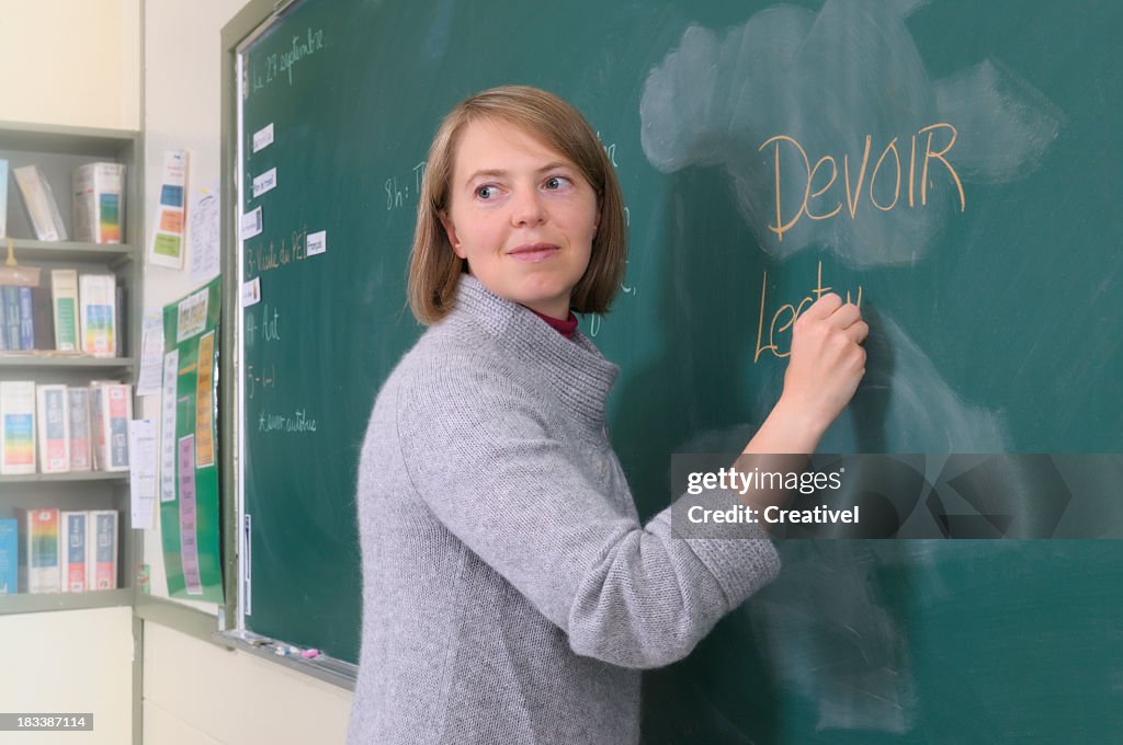 Mature female teacher writing on chalkboard