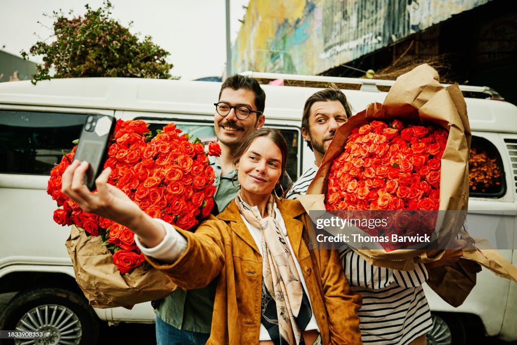 Medium shot friends holding roses taking selfie while visiting market