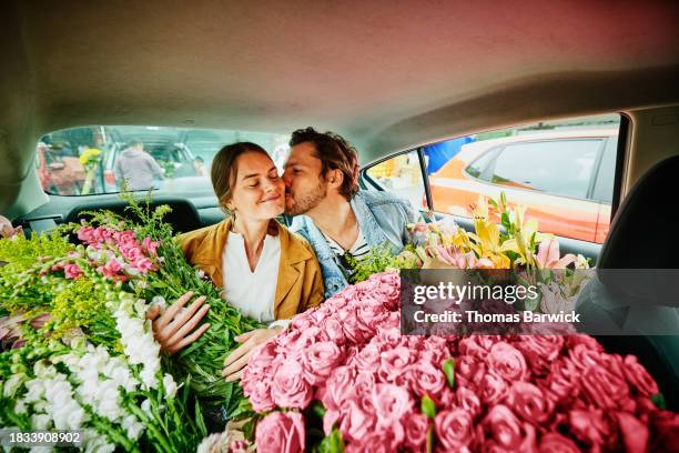 medium shot man kissing girlfriend on cheek in taxi filled with flowers - wange stock-fotos und bilder