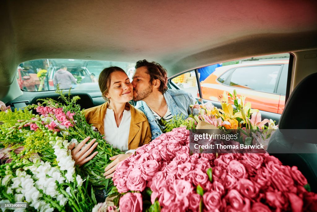 Medium shot man kissing girlfriend on cheek in taxi filled with flowers