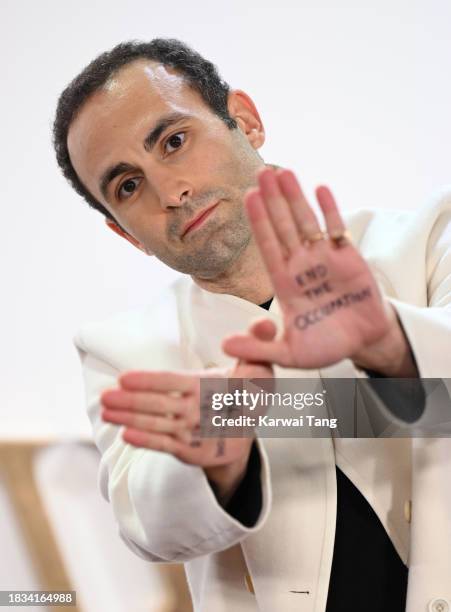 Khalid Abdalla holds up his hands with two messages reading "Return the hostages" and "End the occupation" as he attends "The Crown" Finale...