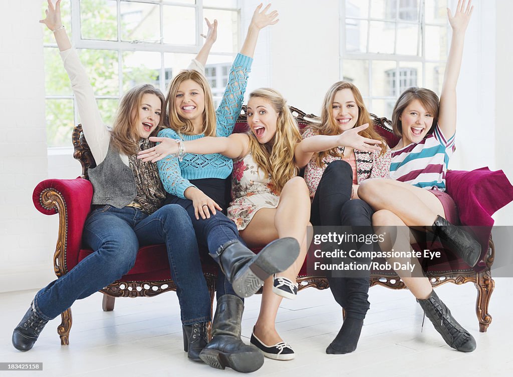 Smiling women sitting on sofa with hands raised