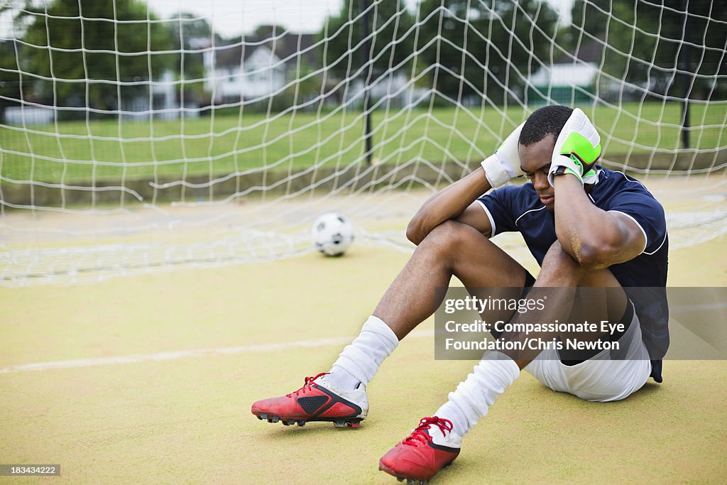 Soccer goalie sitting on pitch with ball in net