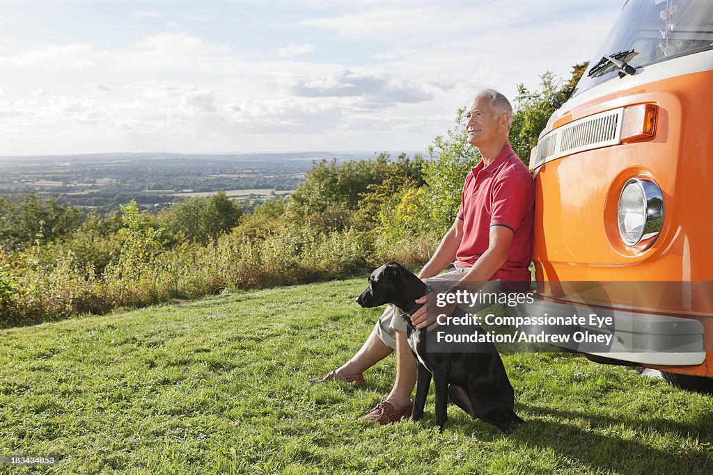 Senior man sitting by camper van with dog