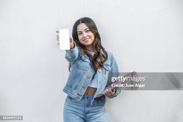 glad female student demonstrating blank screen of cellphone in studio - folder mockup stockfoto's en -beelden