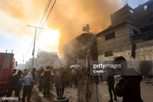 People gather in front of a burning building after it was hit by an Israeli strike in Khan Yunis in the southern Gaza Strip on December 9, 2023....