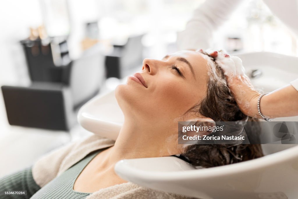 Junge Frau entspannt sich, während Friseur ihre Haare wäscht