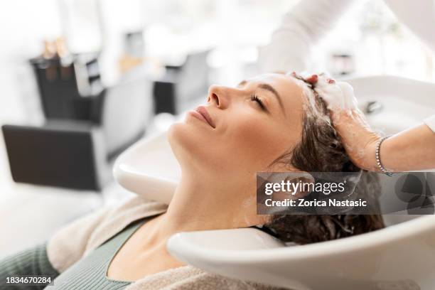 une jeune femme se détend pendant que le coiffeur se lave les cheveux - salon de beauté photos et images de collection