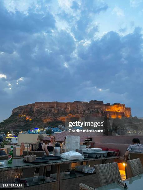 bild des dachrestaurants mit blick über die altstadt und das mehrangarh fort, jodhpur, rajasthan, indien, gebäude und architektur der blue city, blick in die dämmerung, fokus auf den vordergrund - meherangarh fort stock-fotos und bilder