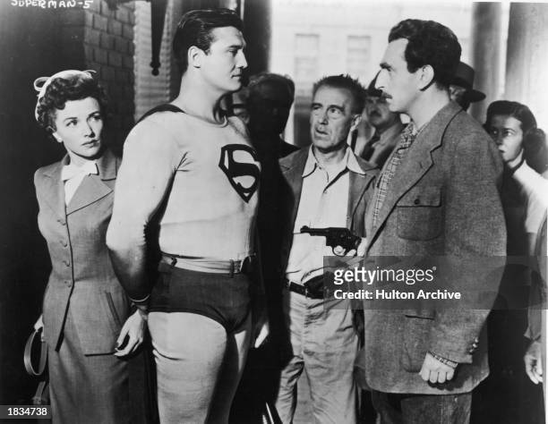 American actor George Reeves , as Superman, stands in front of actor Phyllis Coates, as Lois Lane, while a man points a gun at him in a still from...