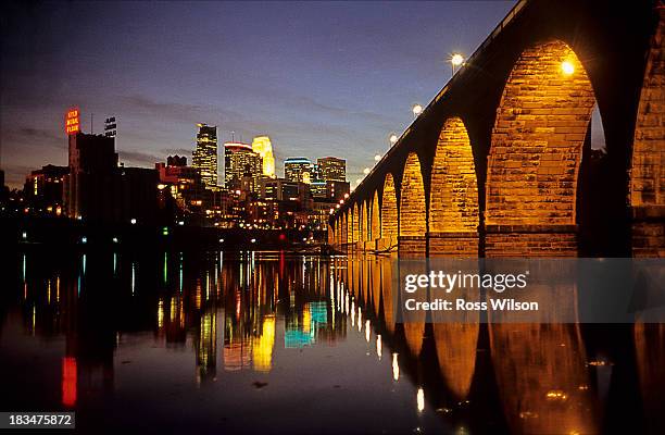 Looking across the Mississippi river and the Stone Arch Bridge to the downtown skyscrapers of Minneapolis at night. The iconic Stone Arch Bridge...