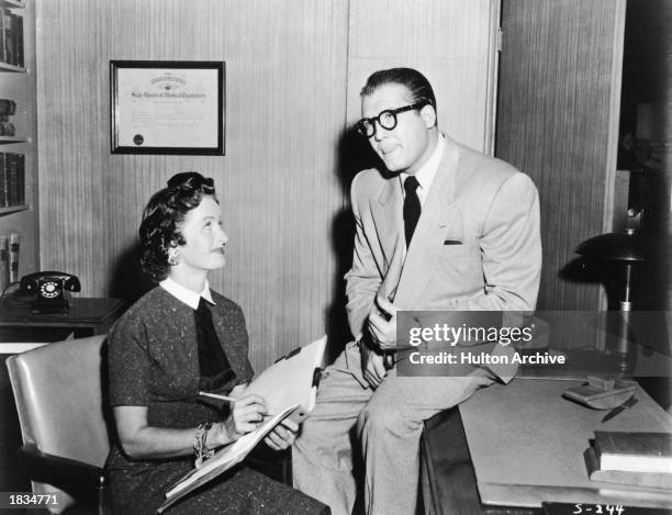 American actor George Reeves , as Clark Kent, sits on desk beside Noel Neill, as Lois Lane, in a still from the television series, 'Adventures of...