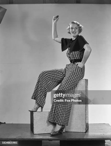 Fashion model wearing wide-leg checkered jumpsuit with capelet and snakeskin print heels, UK, 1935.