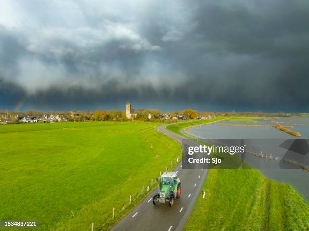 tractor driving on a levee next to the flooded river ijssel with storm clouds - levee stock pictures, royalty-free photos & images