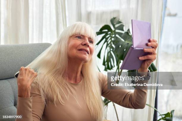 portrait of sitting elderly woman combing her hair in front of a mirror indoors - combing stockfoto's en -beelden