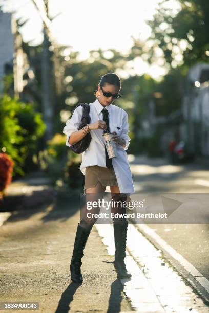 Heart Evangelista wears earrings, sunglasses, golden bracelet from Cartier, a white long shirt from Prada, a black tie from Valentino, a purple woven...