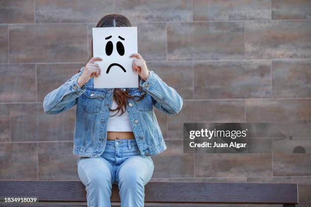 depressed woman covering face with sad smiley - acoso escolar fotografías e imágenes de stock