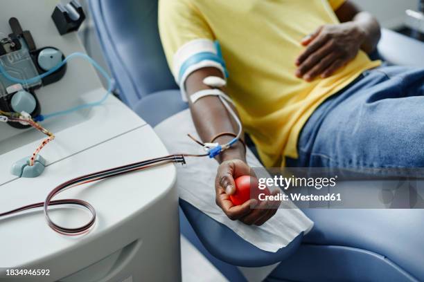 man holding soft ball and donating blood at center - blood donation stock pictures, royalty-free photos & images