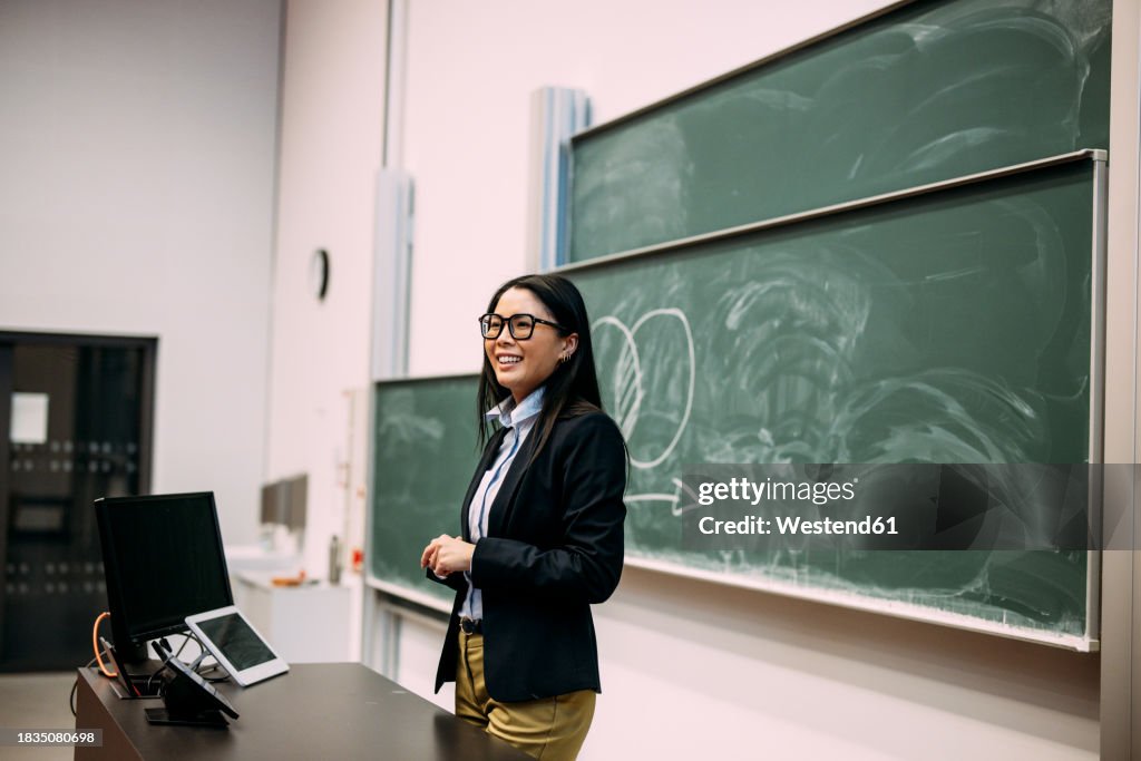Smiling businesswoman standing in front of greenboard at auditorium