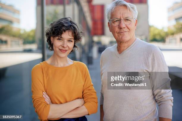 smiling businesswoman standing with senior colleague near building - business park stock pictures, royalty-free photos & images