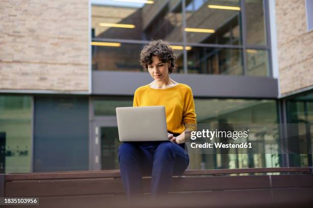businesswoman working on laptop in front of building - büropark stock-fotos und bilder