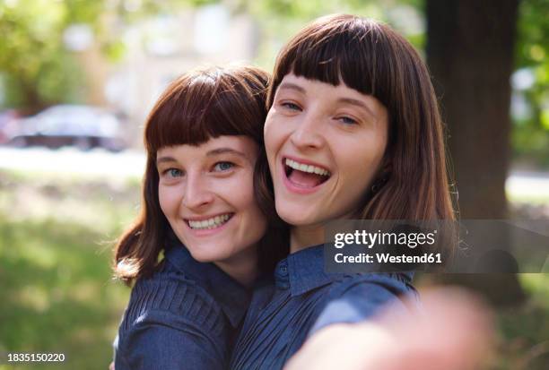 happy twin sisters taking selfie in park - twin stock pictures, royalty-free photos & images