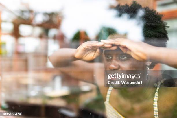 young woman peeking through window - peeking stock pictures, royalty-free photos & images