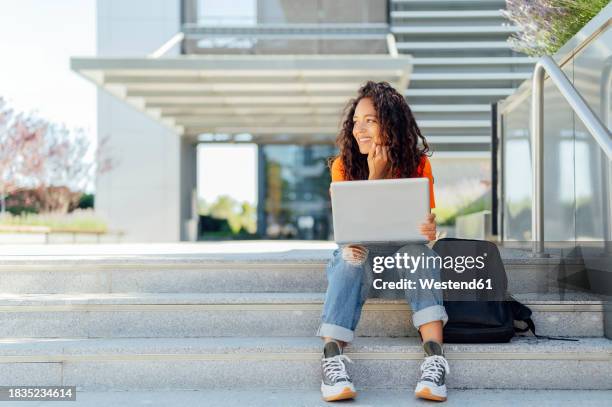 smiling student sitting with laptop on steps in campus - campus fotografías e imágenes de stock