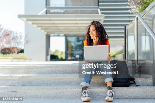 Smiling student sitting with laptop on steps in campus Smiling student sitting with laptop on steps in campus