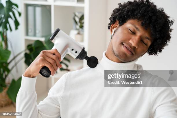smiling freelancer using massage gun at home office - pistolet photos et images de collection